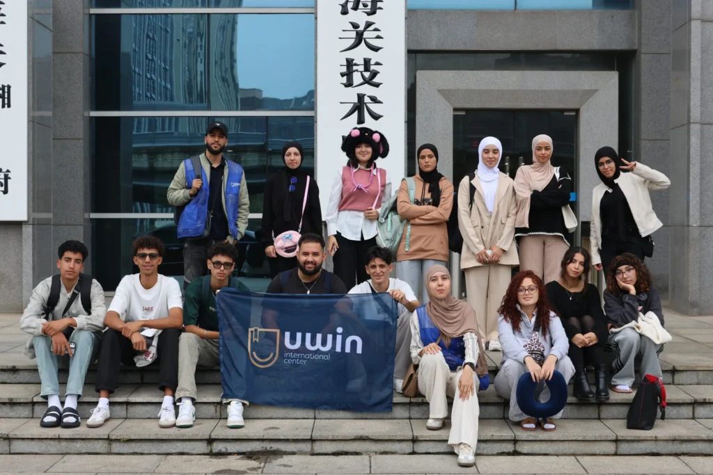 مجموعة من الطلاب المغاربة أمام حرم جامعي في الصين مع علم وكالة UWIN للدراسة في الخارج